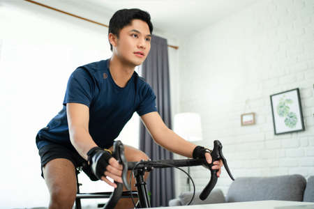 Asian man cycling a bicycle on a trainer at house in the morning. Health and lifestyle concepts.の写真素材