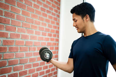 Fit young Asian man in a t-shirt doing a dumbbell workout at home.の写真素材