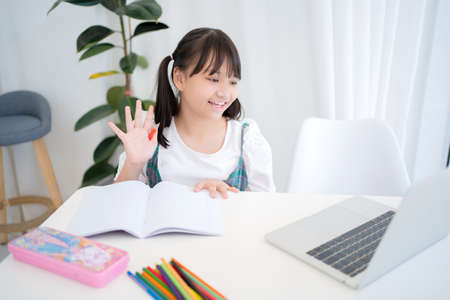 Little children, girls study online at home. She is wearing casual clothes talking on her laptop.