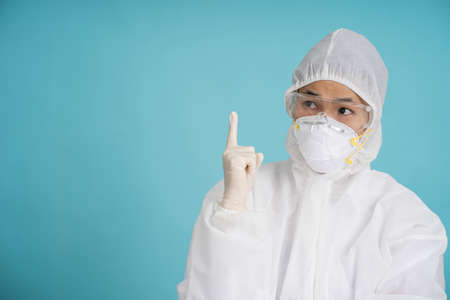 Asian doctors or nurses pointing fingers upward in protective clothing with masks, rubber gloves and goggles.の写真素材