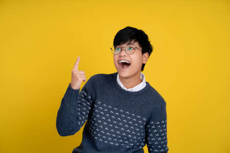 Portrait of a handsome tomboy looking good. Asian woman with short hair on yellow background. She is shocked, gasps and pointing up, isolated background.の写真素材