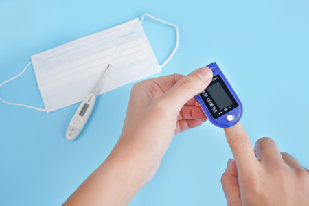 Close up of Finger and hand in an Oximeter Device. Pulse oximeter on a blue background.