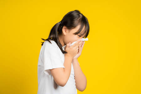 Little asian girl sneeze with napkin paper isolated on yellow background.の写真素材