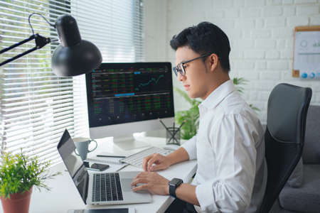 Concentrated young asian modern man in formalwear working using computers while sitting in the office.の写真素材
