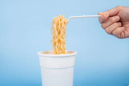 A cup of hot instant noodle on light blue background. Hot instant noodles is a cheap ready to eat food.の写真素材