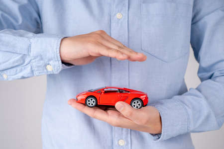 Red car in hands on a white background. Protection of car. Concept of safe driving. Business concept.の写真素材