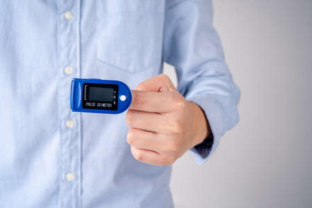 Hand with oximeter, pulse monitoring equipment on grey background.