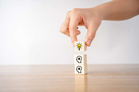 Hand picked wooden cube block with head human symbol and light bulb icon.の写真素材