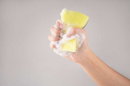 Hand holding yellow sponge for dish wash. Domestic chores and supplies concept. Isolated background.の写真素材
