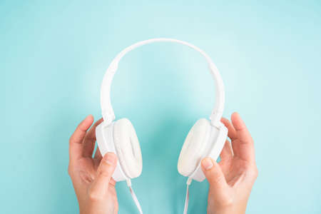 Female hands holding white headphones on blue background.の写真素材