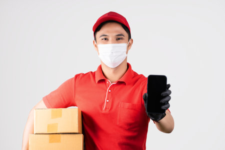 Young male delivery man holding a brown cardboard box and smartphone isolated on white.の写真素材