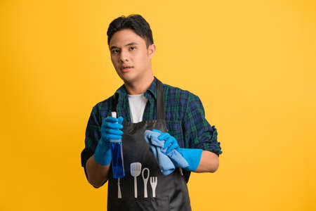 Handsome man with cleaning supplies in hands looking with disgust at camera, not ready for domestic chores, standing on yellow background, Free Spaceの写真素材