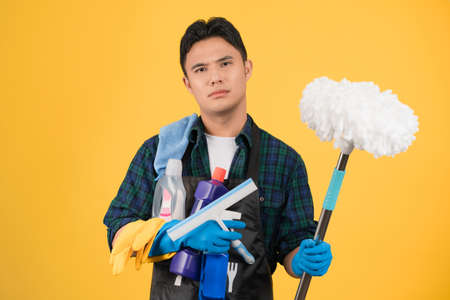 Young Asian man with cleaning supplies on colored background. He is stressed.の写真素材
