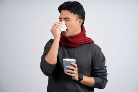 Picture of a sick handsome man wearing a yellow sweater and sneezing. because of influenza virus or...