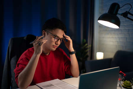 Man sitting in his room working late at night feeling very tiredの素材 [FY310179830473]