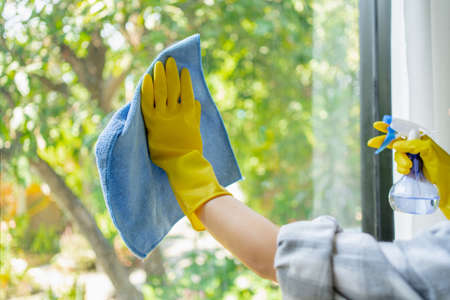 The cleaning staff uses a cloth and dust brush on the window surface with blinds and uses cleaning agents to kill germs and viruses.の写真素材