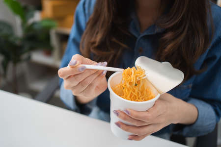 Business woman eating spicy noodles at work place sitting at office with notebook on desk , unhealthy lifestyle eating fast food concept.の写真素材
