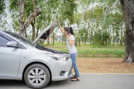 Portrait of young woman standing in front of his broken car, looking at car engine and talking on cell phone, trouble problem mechanic.の写真素材