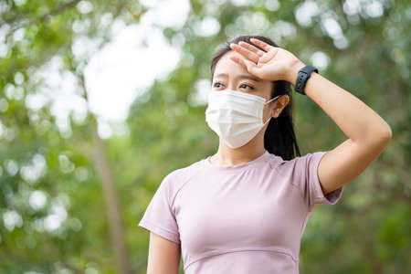 Asian Young fitness sport woman is resting tired and she wears a mask for protective Dust and...
