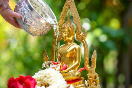 People 's hand using metal bowl to pouring water on golden Buddha statue in Songkran - Thailand famous festival.の写真素材