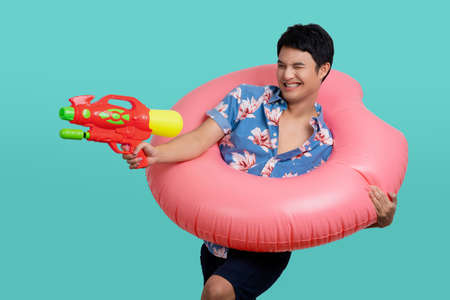 Young tourist man wear beach shirt hold in hand inflatable ring play shoot from water gun isolated...