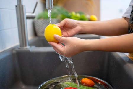 Woman washing fresh lemon in kitchen sink, closeupの写真素材
