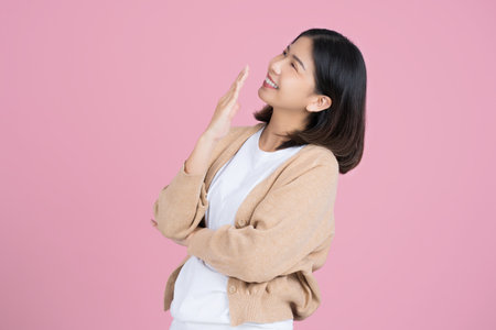 Asian girl wearing a cream colored casual dress, she is surprised standing isolated on a pink background wall.の写真素材