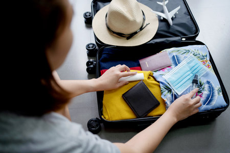 Young woman checking accessories and stuff in luggage at home before travel. Preparing suitcase for summer vacation trip.の写真素材