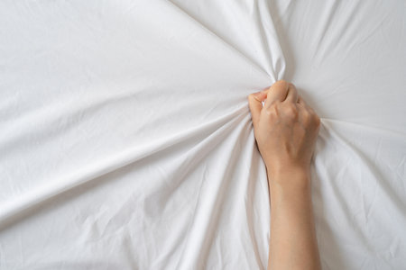 Top view of young sexy woman hands pulling white sheets in orgasm. Sex concept.の写真素材