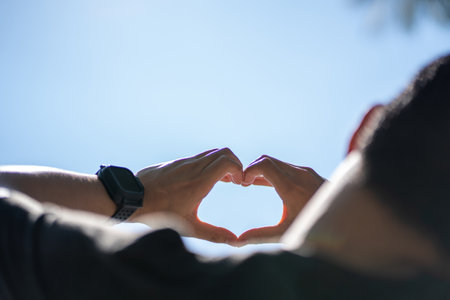 Male hands in the shape of a heart on the sky as background.の写真素材