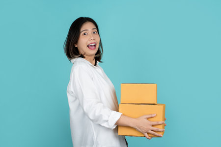 Young Cheerful beautiful asian woman with many parcel cardboard standing on isolated turquoise background.の写真素材