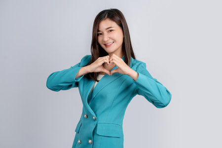 Happy asian business woman in bright green suit showing heart sign with hands isolated on white background.の写真素材