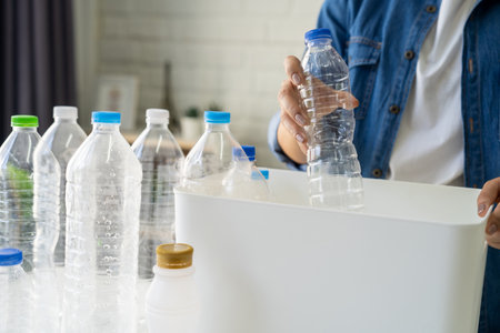 Asian woman separating trash for further recycling at home. She put plastic bottles into recycle...
