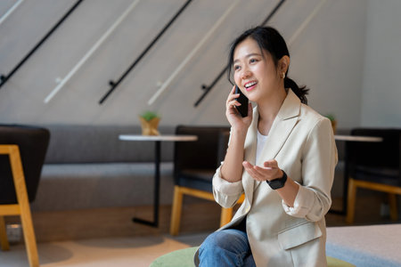 Attractive Asian businesswoman uses smartphone to talk with colleagues while using laptop. Lifestyle concept.の写真素材