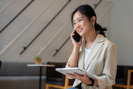 Freelance Asian woman working online at coffee shop, woman talking with customer with mobile phoneの写真素材