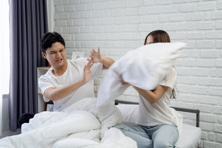 Asian couple in bed arguing on bed at home. They are unhappy and stressed.の写真素材
