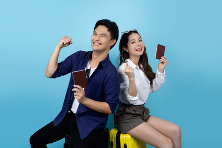Asian tourist couple smiling and raising fists with success, young man sitting on a suitcase.の写真素材