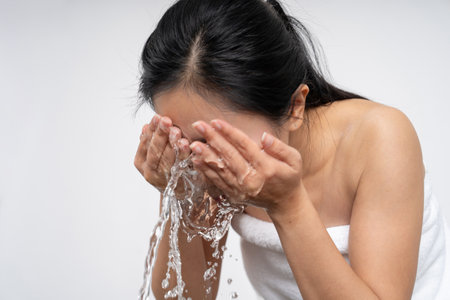 Beautiful young Asian woman washing her face with clean clear water on white background. Skin care concept.の写真素材