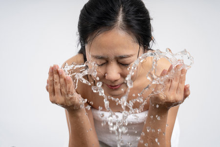 Happy and beautiful natural woman washing face with splashing clean water isolated on white backgroundの写真素材