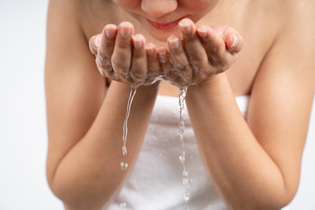Beautiful young woman cleaning her face with fresh water in the morningの写真素材