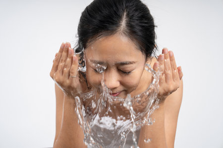 Front view of woman washing face with water in the bathroomの写真素材
