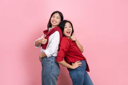 Two happy beautiful Asian girls give thumbs up and look at the camera over a pink backgroundの写真素材