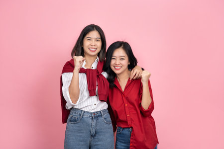 Two Asian girls in red and white shirts are posing smilingの写真素材