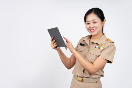 Young woman wearing brown Thai government uniform holding digital tablet computer standing on background,  technology conceptの写真素材