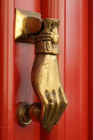 closeup of a hand as a brass door knocker at a red doorの写真素材