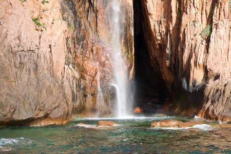 Background of a waterfall in front of a red cliff into the seaの写真素材