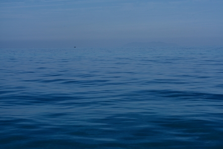 One ship far away on the endless blue ocean, all under a blue skyの写真素材