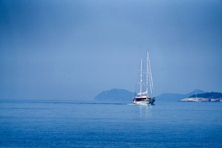 White sailing boat in front of the croatian coastlineの写真素材