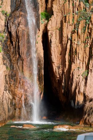 Waterfall into green water in front of red rocksの写真素材