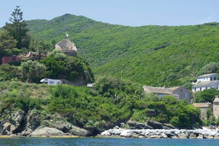 Ruin of a Genoese tower with some homes at the seaの写真素材